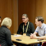 Vier Personen sitzen in einem holzvertäfelten Seminarraum bei einem Coaching.