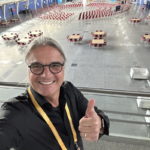 Michael Muench zeigt Daumen hoch in einer großen Halle vor einem Seminar für Unternehmensentwicklung.